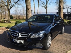 Schwarzer Mercedes Benz als Limousine auf dem Parkplatz vor einem Restaurant.